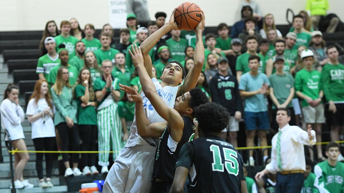 Justin Mckoy, left, of Panther Creek drives to the basket against Jared Moore, center, and Bryan Quiller (15) of Cary. The Panther Creek Catamounts played the Cary Imps in a high school men basketball game on February 26, 2019.