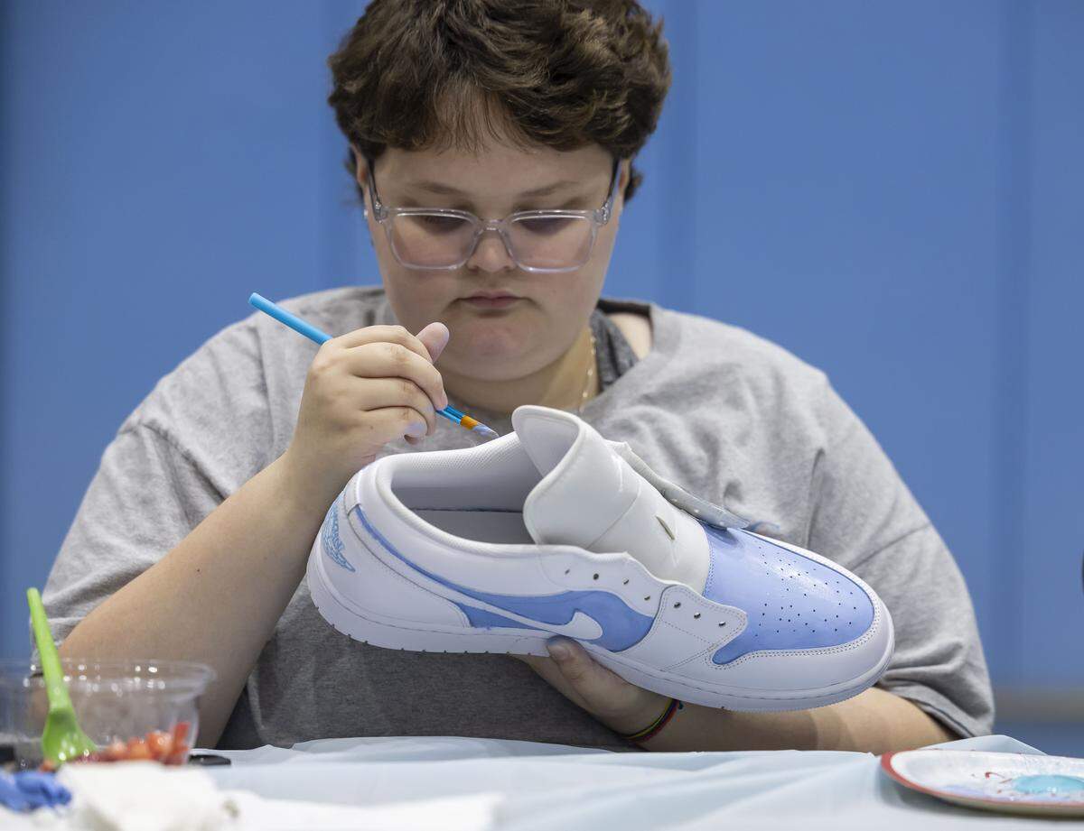 Riley Darcy of Burlington, carefully paints a pair of size 18 shoes for North Carolina coach Sean May, during the Shoes 4 Hope event.