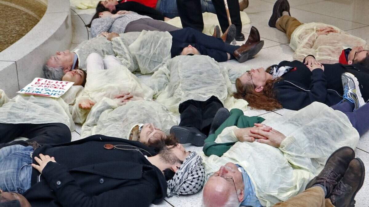 Rev. William Barber, head of the NC NAACP, standing, prays over 13 protesters who participated in a die-in at under the rotunda of the NC Legislature Thursday afternoon, February 12, 2015. The protestors were rallying to protest the state’s continued denial of Medicaid expansion for hundreds of thousands of North Carolinians. The protesters were from the NC NAACP and the Forward Together Moral Movement.