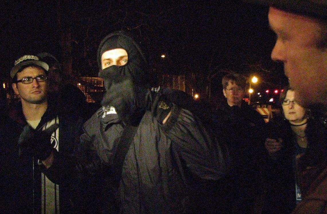 A masked demonstrator who gave his name as Johnny Moran and called himself an anarchist speaks outside the building at Greensboro and Weaver streets that a group of demonstrators briefly occupied Saturday to protest a planned CVS store in downtown Carrboro. To the right is Carrboro Police Chief Carolyn Hutchison, and Mayor Mark Chilton (far right in profile) listen. No arrests were made when the protesters obeyed the mayor and police instructions to leave or be arrested.