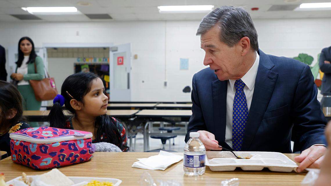 Gov. Roy Cooper speaks with kindergarten student Sankeerthana Lolla while eating lunch at Bethesda Elementary School on Tuesday, Oct. 11, 2022, in Durham, N.C. Cooper visited the school to announce new agreements to bring food from North Carolina farmers and producers to schools.
