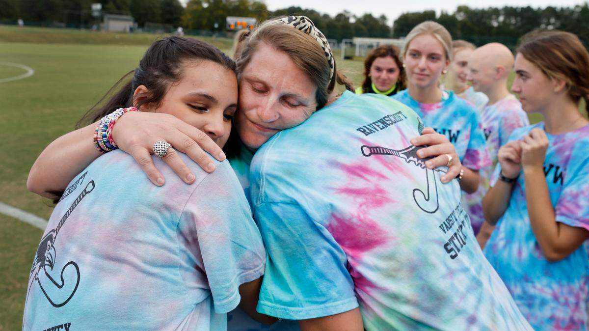 Whitford Wooten, an assistant field hockey coach at Ravenscroft High School, gets a hug from Kiara Irvine and Claire Anysz after Wooten was honored during a ceremony before their game with St. Mary’s School Tuesday, Oct. 10, 2023. Wooten has ALS (amyotrophic lateral sclerosis or Lou Gehrig’s disease), a progressive neurodegenerative disease.