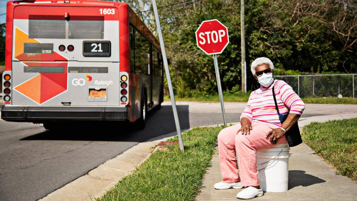 Lenora Southerland, 82, poses for a portrait at the bus stop near her Raleigh home on Wednesday, April 14, 2021. There isn’t a bus shelter or seating so Southerland has to sit on a bucket to wait for a bus due to her knee pain.