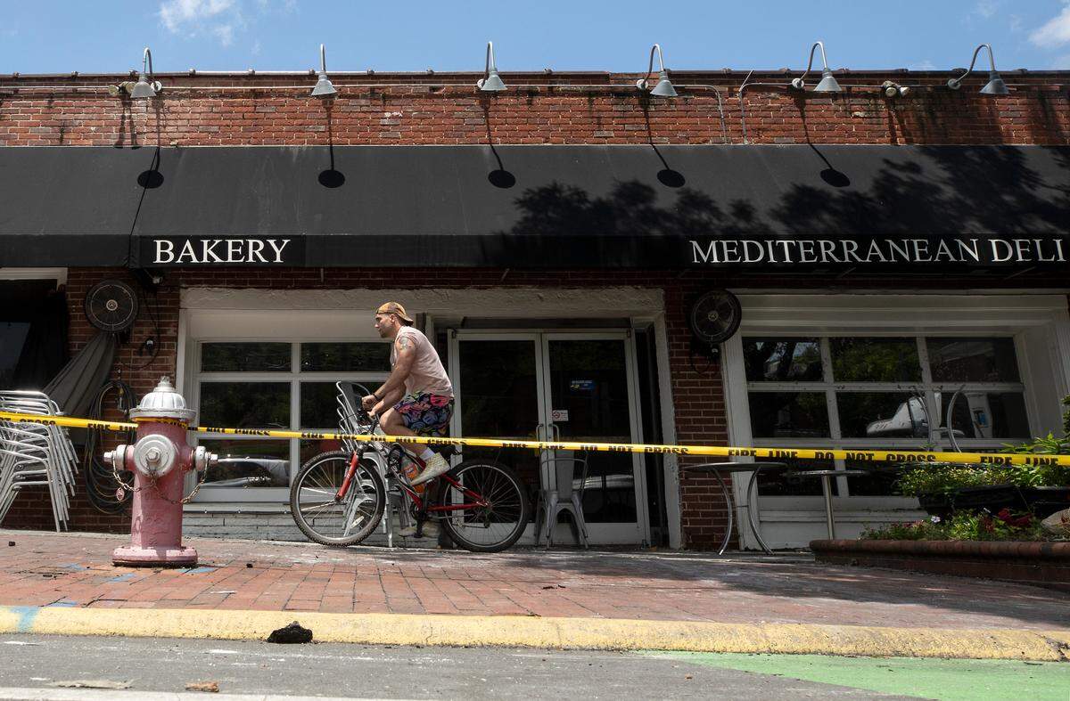 A person rides a bicycle past caution tape in front of Mediterranean Deli, Bakery and Catering on Monday, July 24, 2023, following a Saturday fire at the Chapel Hill business.