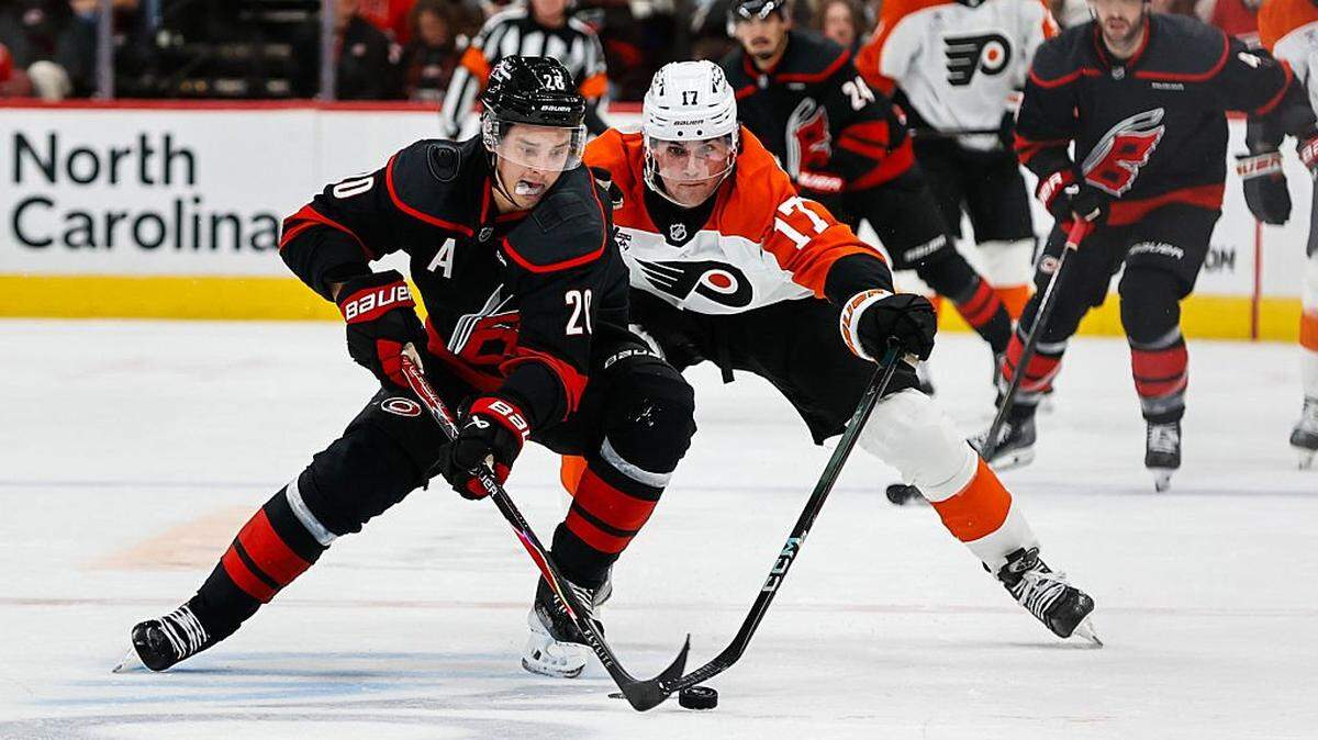 Jett Luchanko (17) of the Philadelphia Flyers and Sebastian Aho of the Carolina Hurricanes vie for the puck during the first period of the game at Lenovo Center on October 11, 2025 in Raleigh, North Carolina.