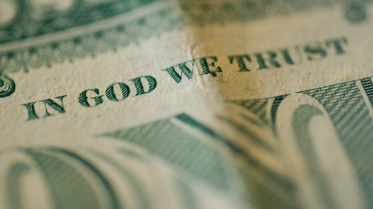 A close up shot of rolled up American bills. Focus on “In God We Trust”