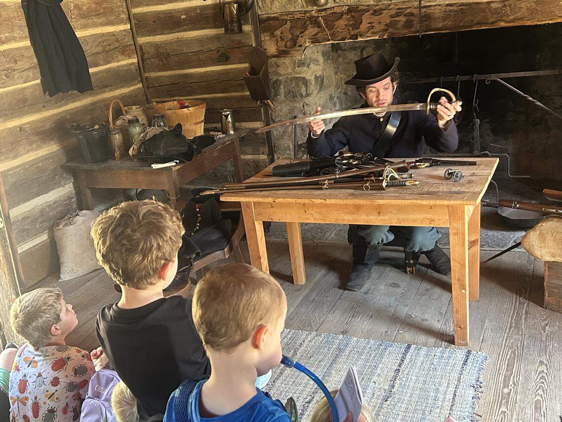 Historical interpreter Tyler Mink shows a cavalry saber to students attending a Homeschool Day at Bennett Place State Historic Site in Durham on Friday.
