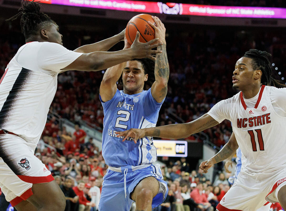 North Carolina’s Elliot Cadeau drives between N.C. State’s DJ Burns Jr. and Dennis Parker Jr. during the first half of the Tar Heels’ 67-54 win at PNC Arena on Wednesday, Jan. 10, 2024, in Raleigh, N.C.