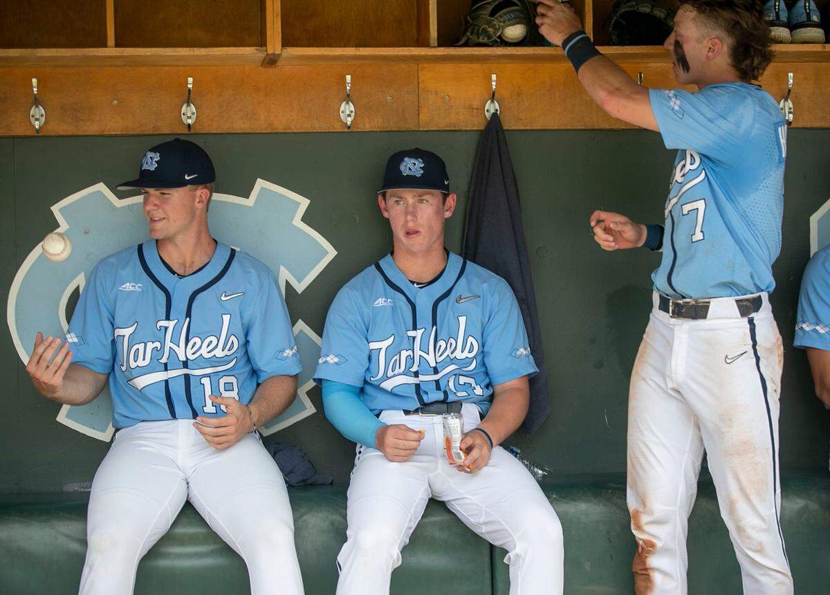 North Carolinas Clemente Inclan (18), Joe Jaconski (17) and Vance Honeycutt (7) take cover in the Tar Heels dugout during a weather delay in the bottom of the second inning during their NCAA Super Regional series game against Arkansas on Sunday, June 12, 2022 at Boshamer Stadium in Chapel Hill, N.C.