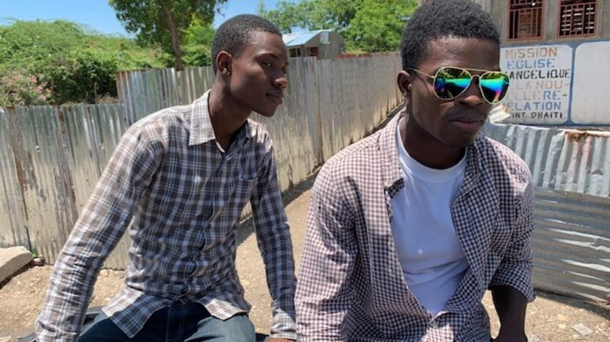 Daphno Aristile (left) and Jonas Vertus ride in the back of a pickup truck on an unpaved road outside a church in the Gonaives area of Haiti.