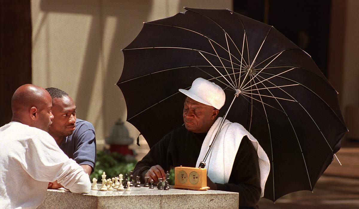Keldric Nicholson (center)  and Mr. Mike (no kidding) watch as the umbrella-shaded Sherman Leathers ponders a move  during a lunchtime chess match on the mall near the Convention Center on May 21, 1999. 