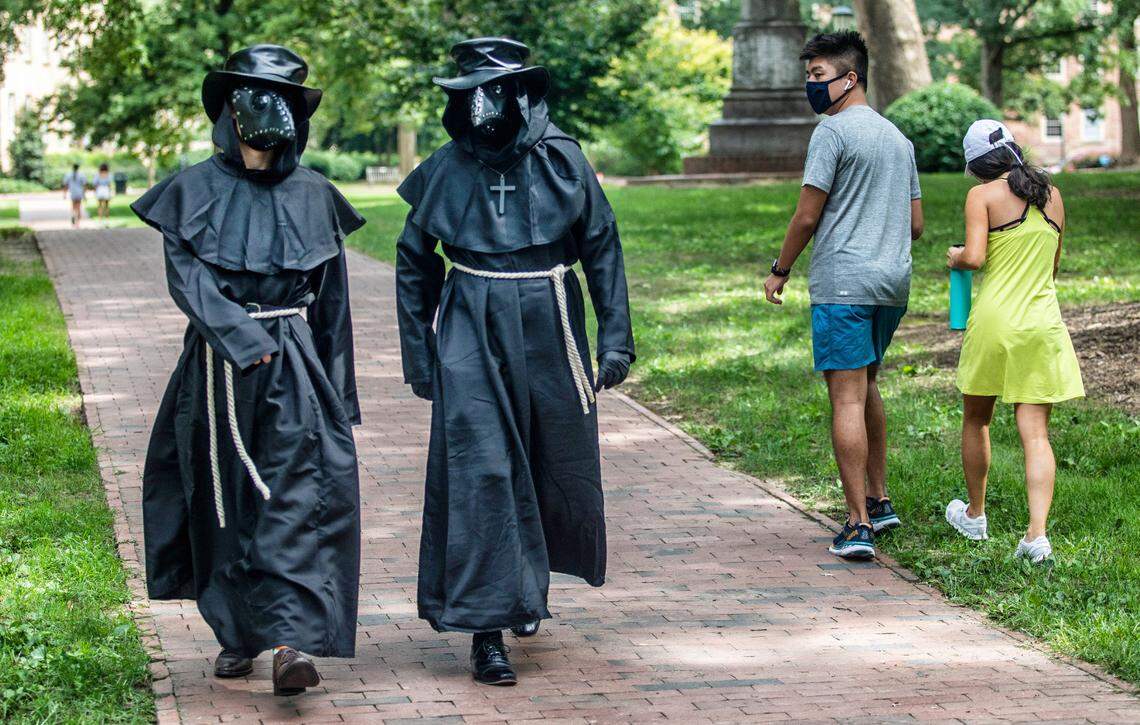 A passerby reacts as Stefano Dongowski (left) and his friend who did not want to be identified, walk on the UNC campus dressed as “plague doctors” in an effort to encourage students to wear masks Friday Aug. 21, 2020. The university cancelled in person classes due to COVID-19.