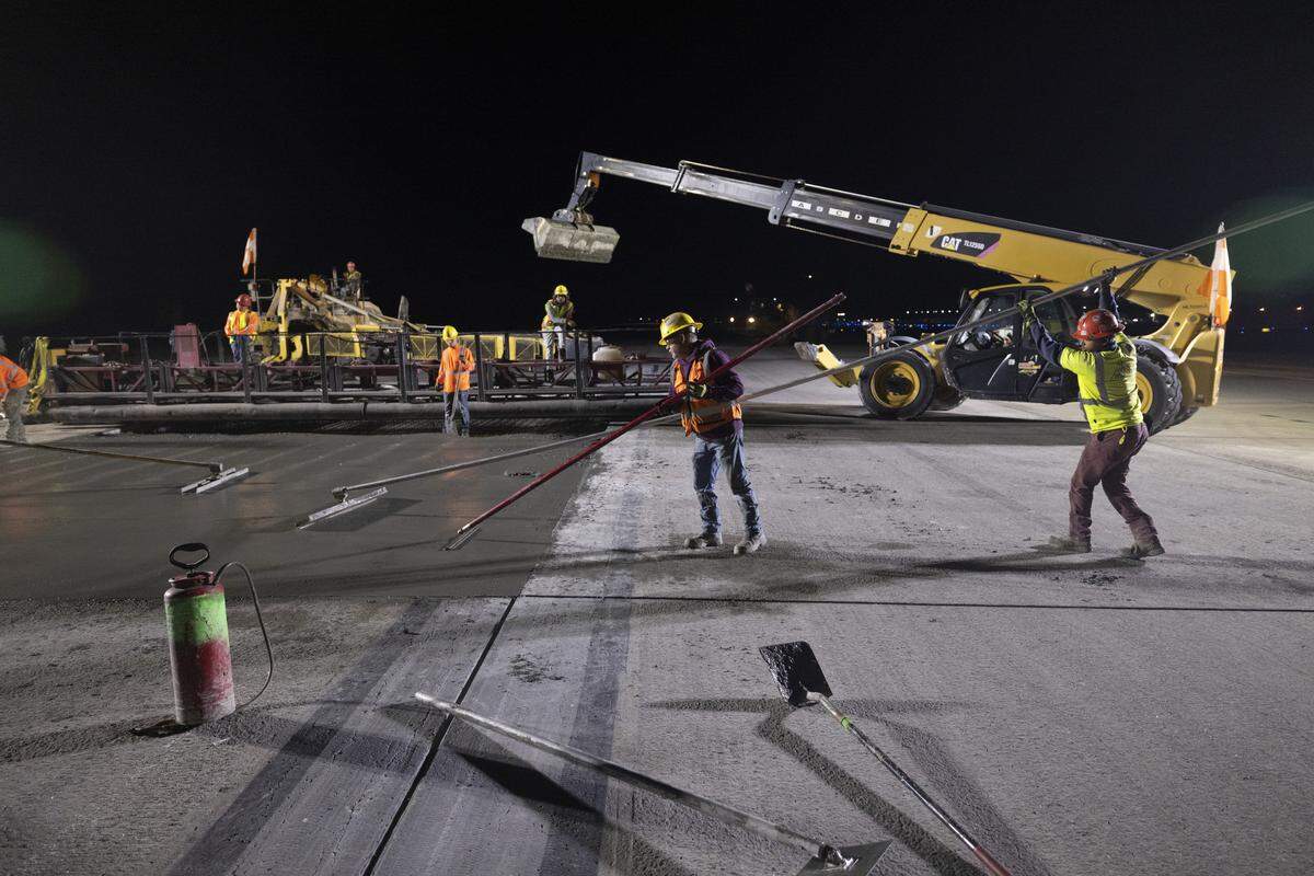 Hi-Way Paving employees use tools called bull floats to smooth the fresh concrete in the runway. The triple tube roller machine, seen in the back, does most of the smoothing work.