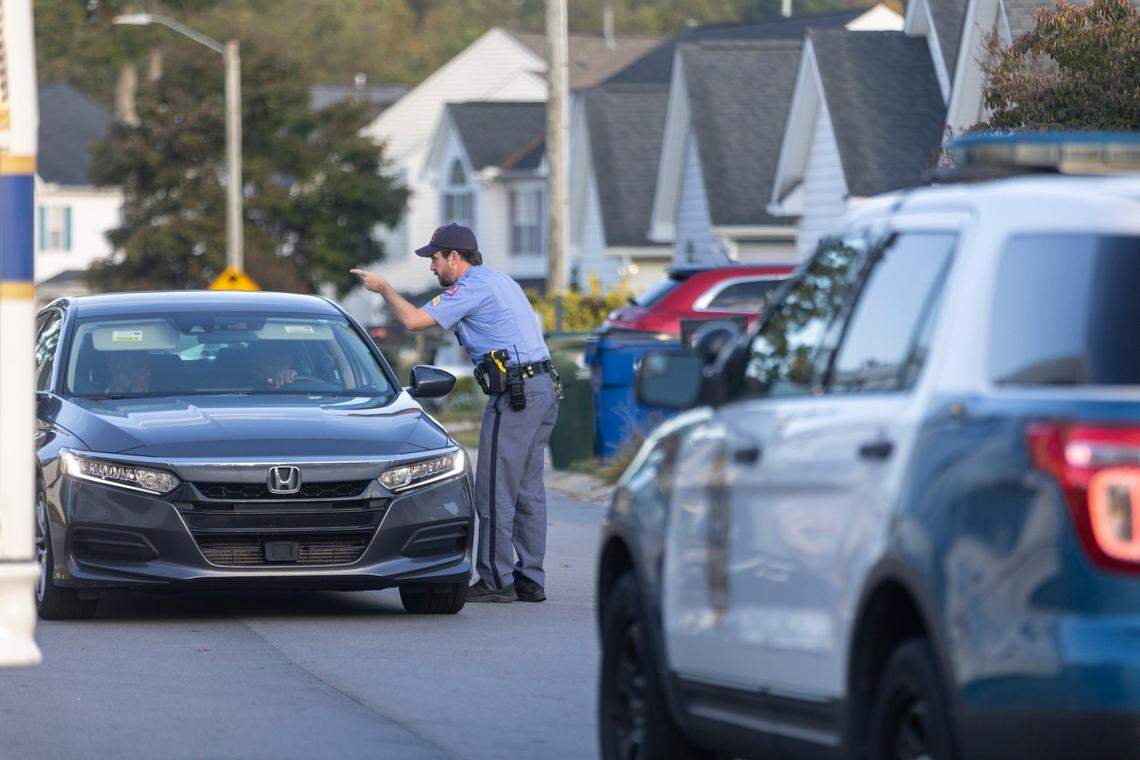 Raleigh police direct a motorist on Castle Pines Drive in the Hedingham neighborhood on Friday morning, October 14, 2022 in Raleigh, N.C. as they continue to investigate the killing of five people yesterday on the greenway nearby.