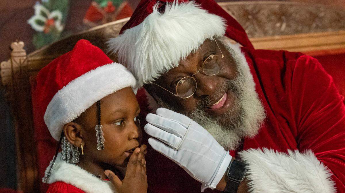 Nai’lah McCullers, 4, whispers her Christmas list while having her photograph taken with Santa Claus, aka Joe Griffin, or Santa Joe, at the Hayti Heritage Center in Durham Wednesday, Dec. 21, 2022.
