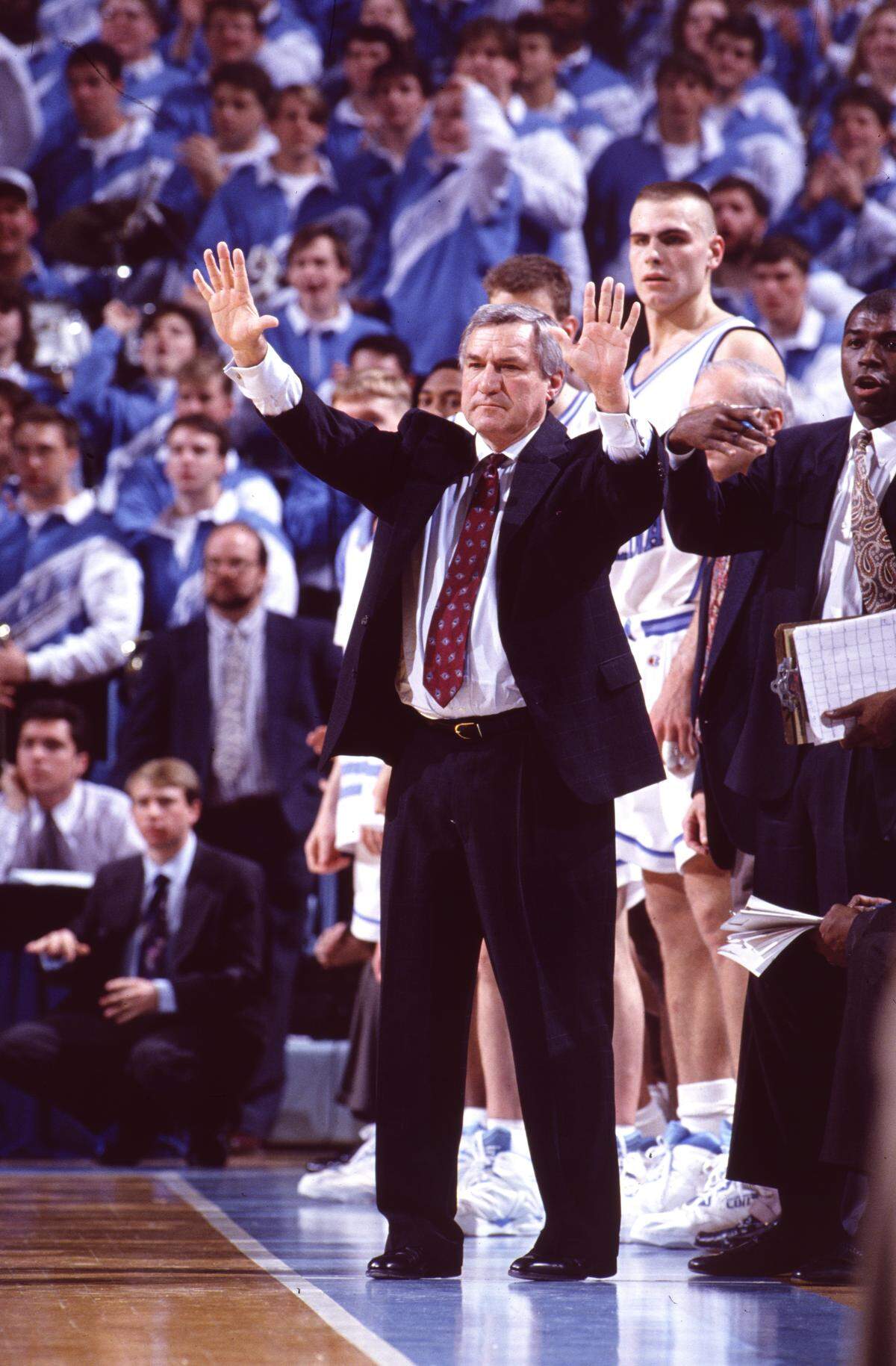 UNC coach Dean Smith works the sidelines of a game in the Smith Center.  Center Eric Montross is in the background, and former player and assistant Phil Ford at right.  