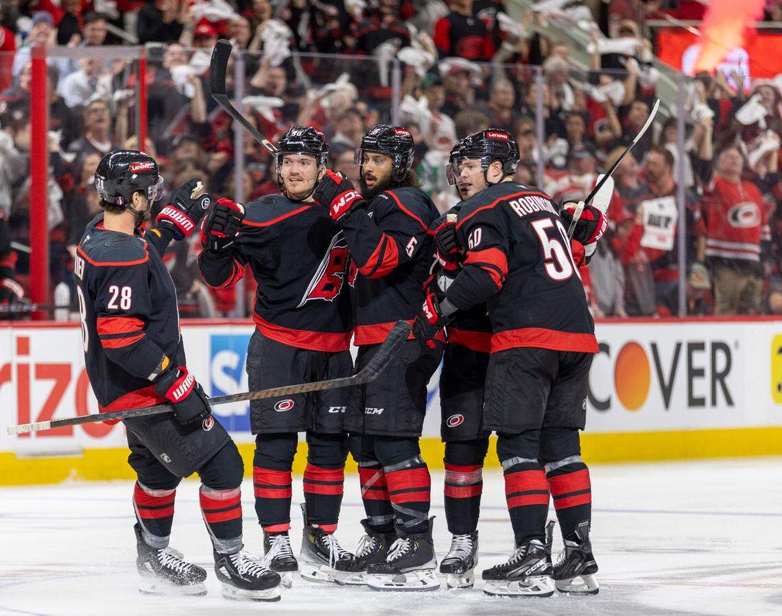Carolina Hurricanes defenseman Jalen Chatfield (5) is surround by teammates William Carrier (28), Jack Roslovic (96) and Eric Robinson (50) after he scored to give the Hurricanes a 1-0 lead against the New Jersey Devils in the first game of the playoffs on Sunday, April 20, 2025 at Lenovo Center in Raleigh, N.C.