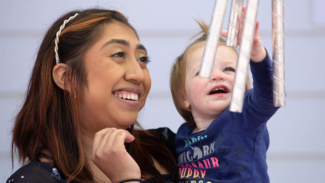 Roxanna Campos-Sosa, a teacher at the Little School of Hillsborough, watches as Mackenzie, 1, plays with wind chimes on Thursday, April 18, 2024, in Hillsborough, N.C.