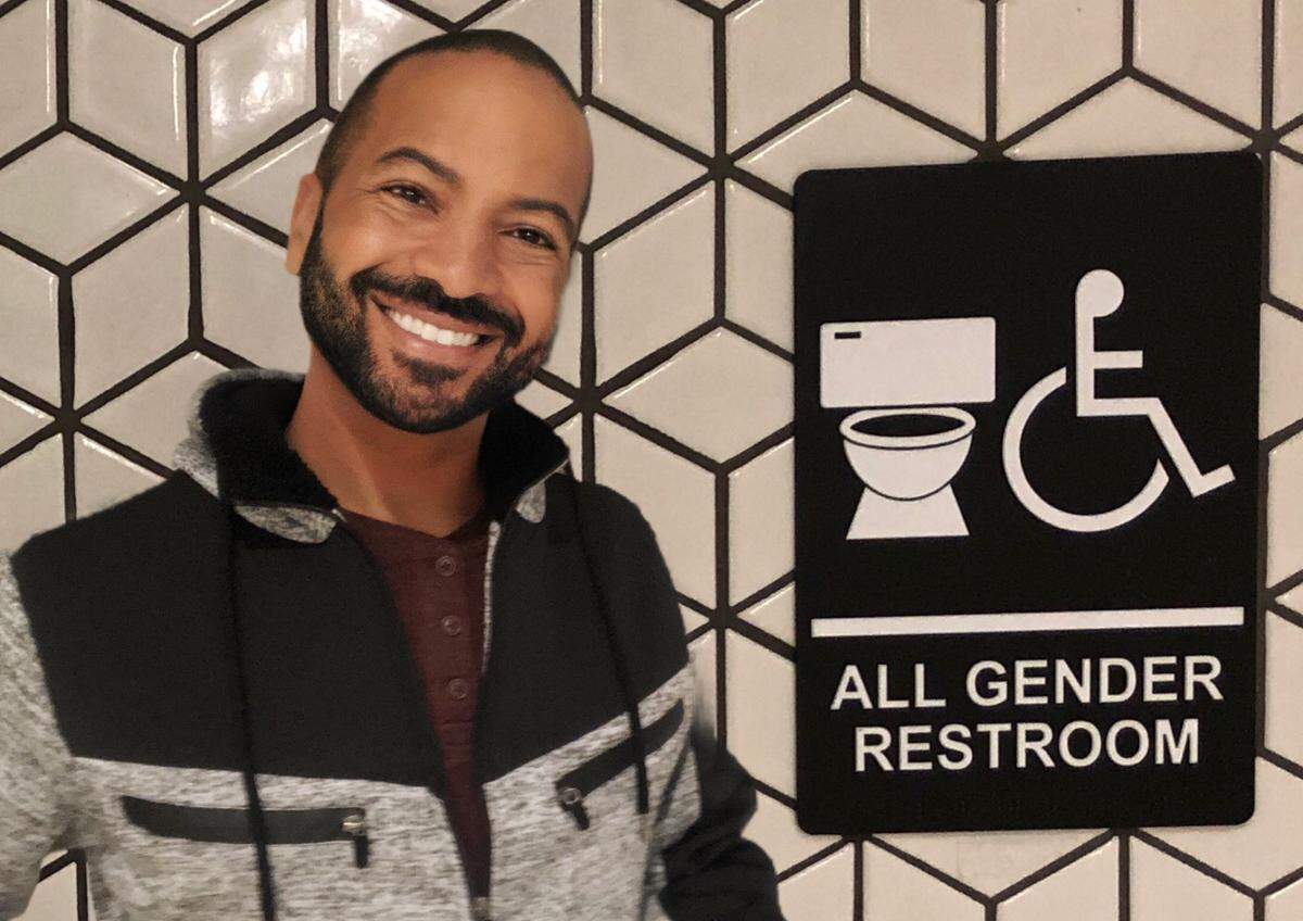 Devin Pearson, a non-binary author of children’s books, stands by an “all gender restroom” sign outside a bathroom at Crabtree Valley Mall. Pearson pushed the mall to make its single-occupancy bathrooms available to anyone who needed to use them after they were repeatedly refused access to one during a visit to the mall in August.