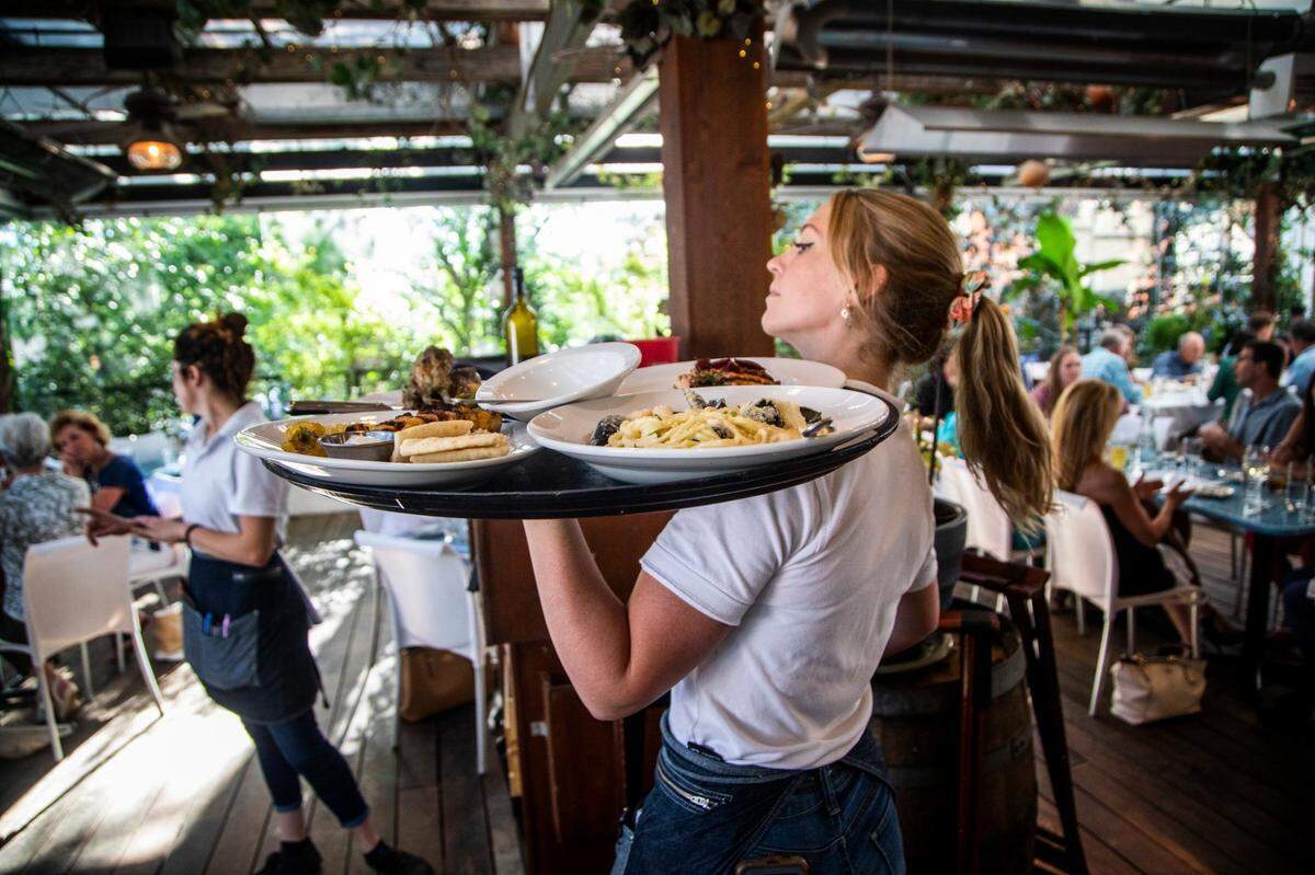 Server Charlotte Jones takes food to diners Wednesday, June 16, 2021 at Taverna Agora Greek Kitchen & Bar in Raleigh. Many restaurants say business is starting to return to normal as coronavirus restrictions have lifted but hiring remains a challenge.