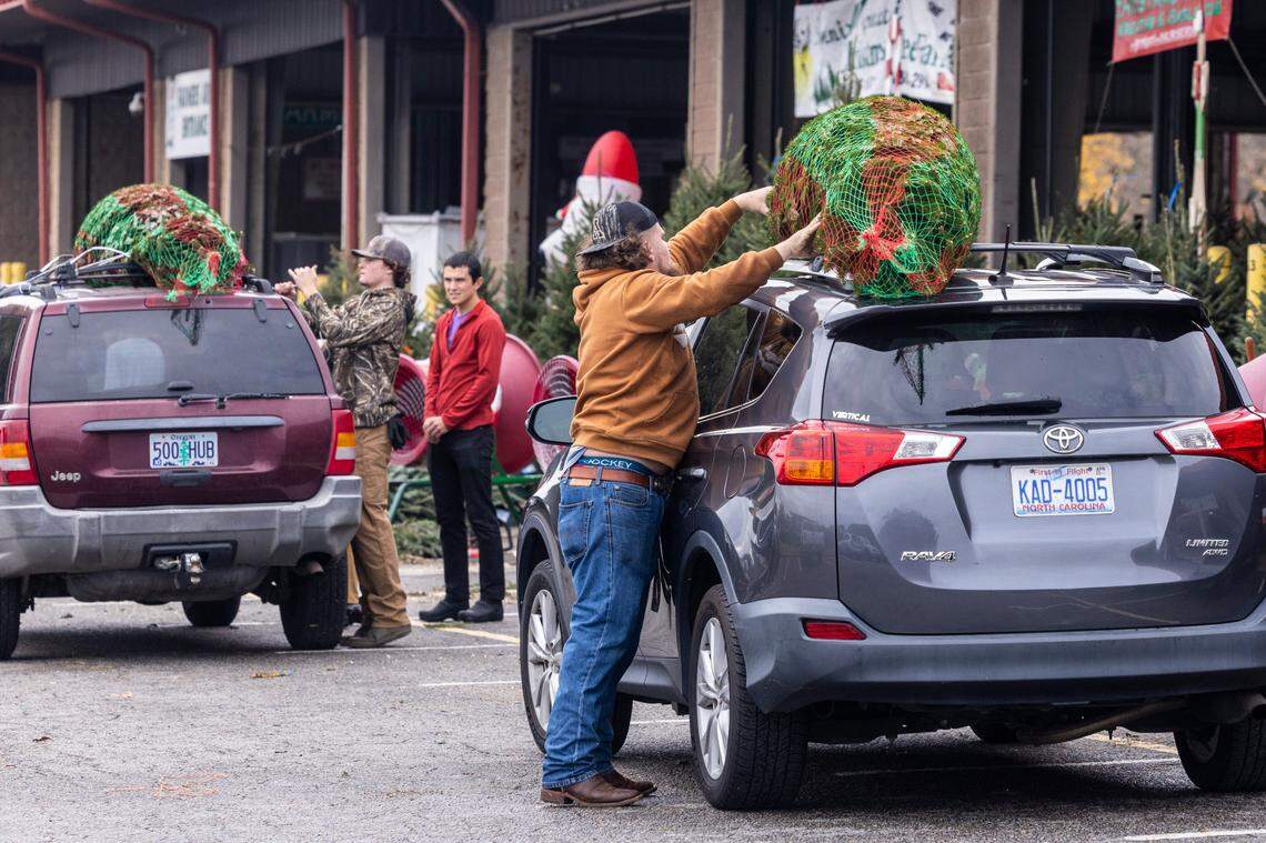 Christmas tree farm workers strap trees to the roof of cars at the State Farmers Market in Raleigh Friday, Nov. 25, 2022. The market was busy with families buying Christmas Trees after the Thanksgiving holiday.