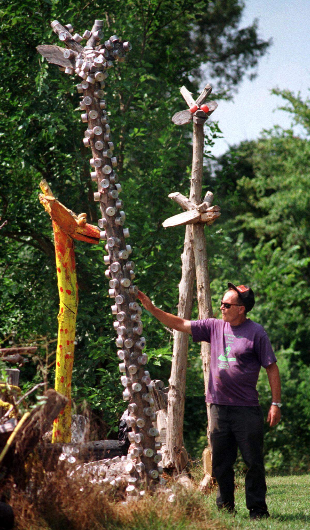 Chain saw sculptor Clyde Jones wanders by some of his taller chainsaw creations in his backyard. Jones says he prefers cedar to make his sculptures.