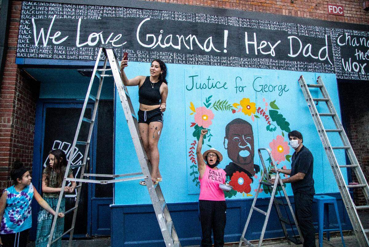 Owners and workers of Centro restaurant cheer on about 100 protesters as they march past curfew in downtown Raleigh Wednesday, June 3, 2020. The group was finishing up a mural on the boarded up restaurant after it was vandalized during protests over the weekend.