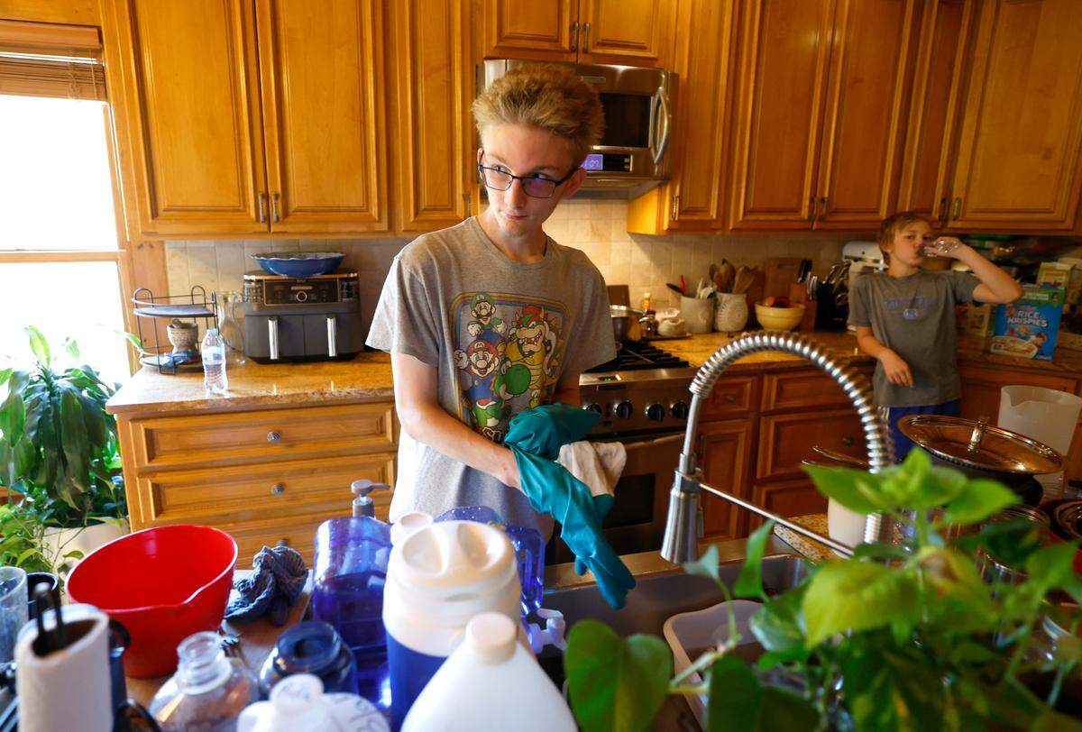 Evan Bloemendaal, 17, washes dishes with water from a two gallon container in their home in Banner Elk, N.C., Wednesday, Oct. 9, 2024. The Bloemendaal’s power has been restored but there is no estimate on when they will get water back.