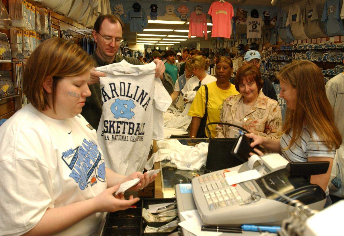 Carolina Pride employee Courtney Lewis, left, works the cash register as Chris Belcher folds another freshly printed UNC 2005 National Champions T-shirt for customer Tracy Jackson of Carrboro, right, during the post-championship morning crush of shoppers to Franklin Street stores.