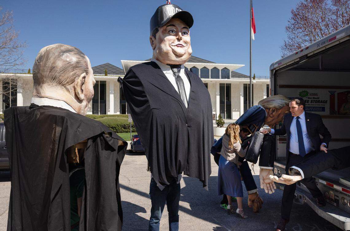 State Sen. Graig Meyer (right, carrying arms) helps unload giant puppets of Russian President Vladimir Putin, Elon Musk, and President Donald Trump before a March 12, 2025 rally opposing cuts by DOGE and Musk.
