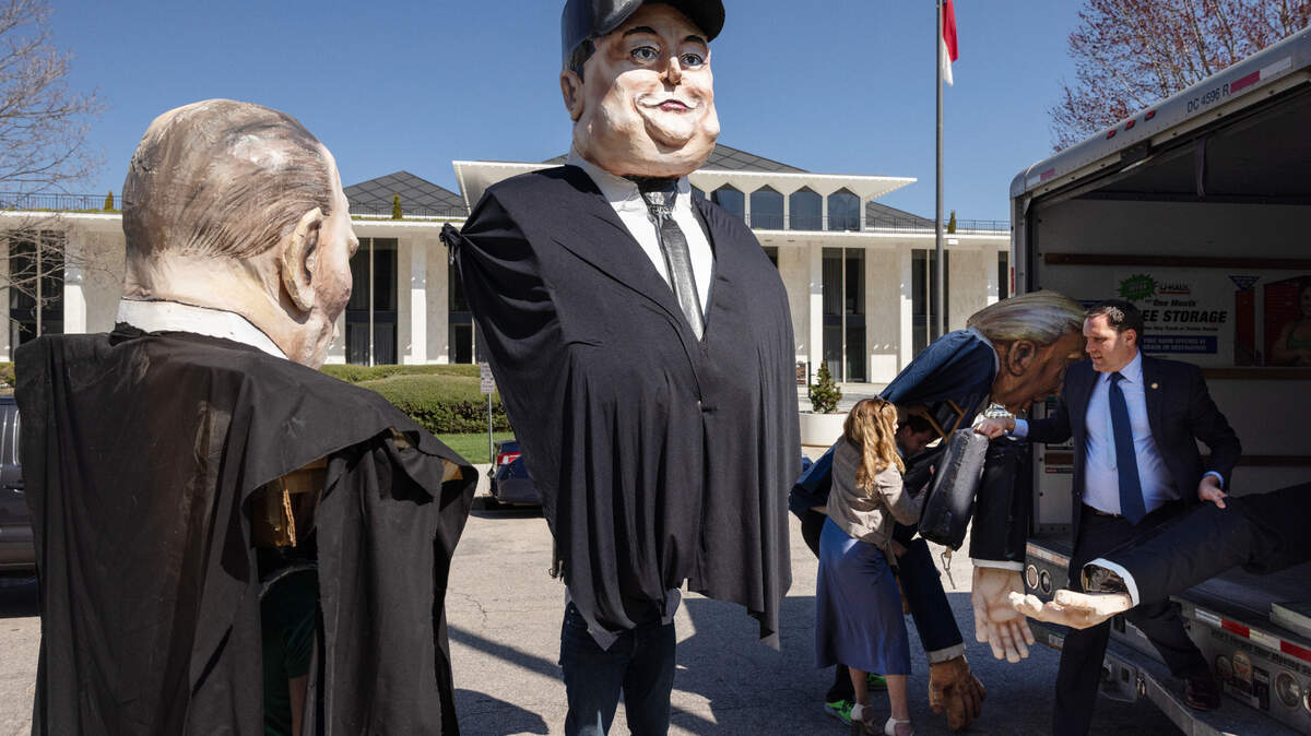 State Senator Graig Meyer (right, carrying arms) helps unload giant puppets of Vladimir Putin, Elon Musk, and President Donald Trump before a March 12, 2025 rally opposing cuts by DOGE and Musk.