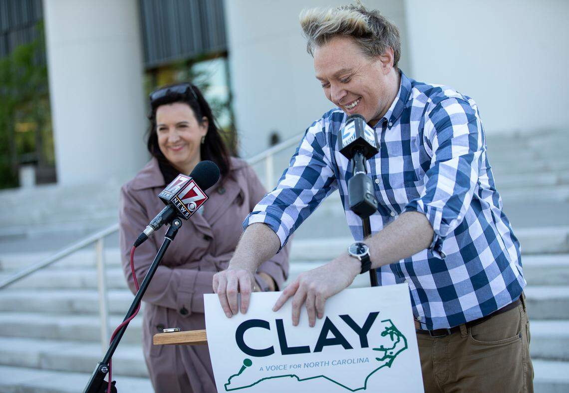 Clay Aiken, a Democratic candidate for North Carolina’s 4th Congressional District, takes a DIY approach and reattaches his campaign poster to the podium following remarks by Ashley Ward, a Democratic candidate for the same district, during a press conference on Wednesday, May 11, 2022, in Durham, N.C.