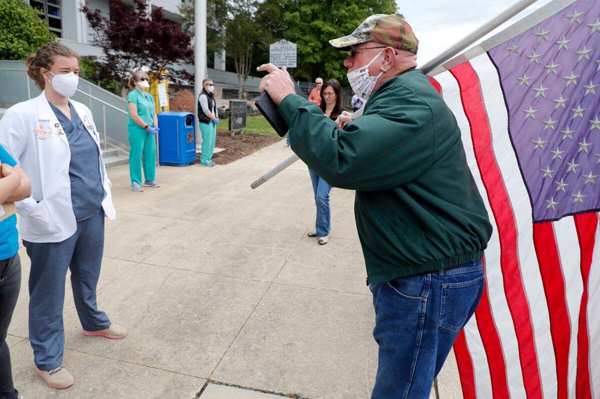 A protester, who did not want to give his name, yells at medical student Carrie Shropshire and others during the ReOpenNC protest in downtown Raleigh, N.C., Tuesday, April 21, 2020.