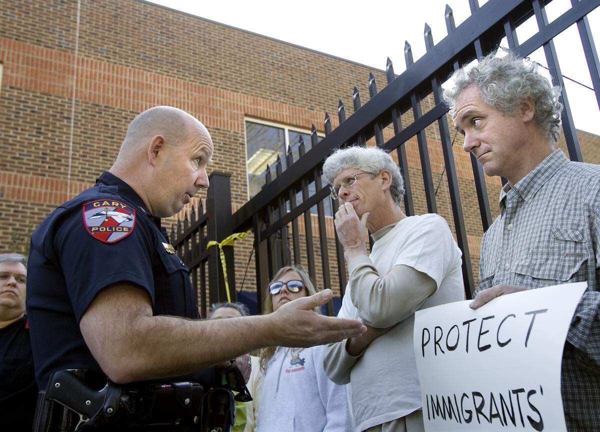 Cary Police Sergeant R.C. Swallow, left,  talks to protesters Patrick O'Neill of Garner, center, and Steve Woolford, 42, of Silk Hope, right, outside the Immigration and Customs Enforcement detention facility in Cary. About 40 people demonstrated. There were no arrests.