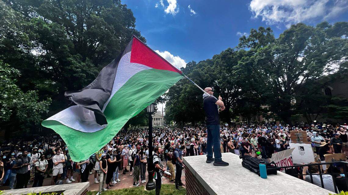 A pro-Palestinian protester holds a large Palestinian flag by the steps of South Building during a noon rally on campus. The rally followed arrests that morning of protesters occupying an encampment on campus.