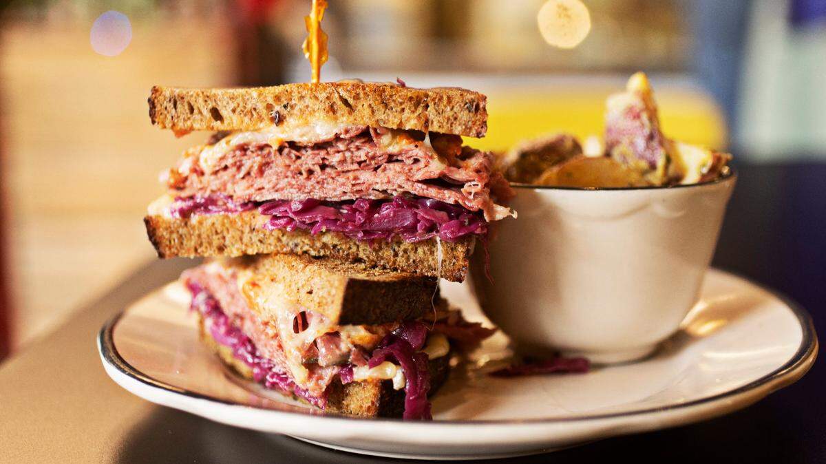 Raleighs (ish) delicatessen makes a housemade pastrami or corned beef sandwich with Swiss, Super Russian, braised purple cabbage, on Boulted Bread rye. It is served here with a side of potato salad made with charred onions and dressed in olive oil and mustard.