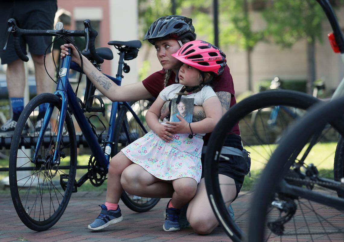 Tatiana Allore sits with Valkyria, 3, prior to the Ride of Silence on Wednesday, May 17, 2023, in Durham, N.C. Valkyria holds a photograph of John Allore, who was killed after a car struck his bike in March. The Ride of Silence remembers those who were killed or injured while biking.