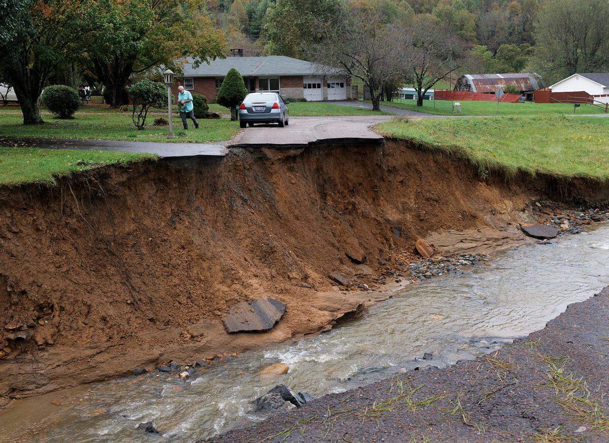 A person walks by a section of washed out road near Highway 421 in Boone, N.C., days after Hurricane Helene brought heavy rain and flooding to the western part of the state.