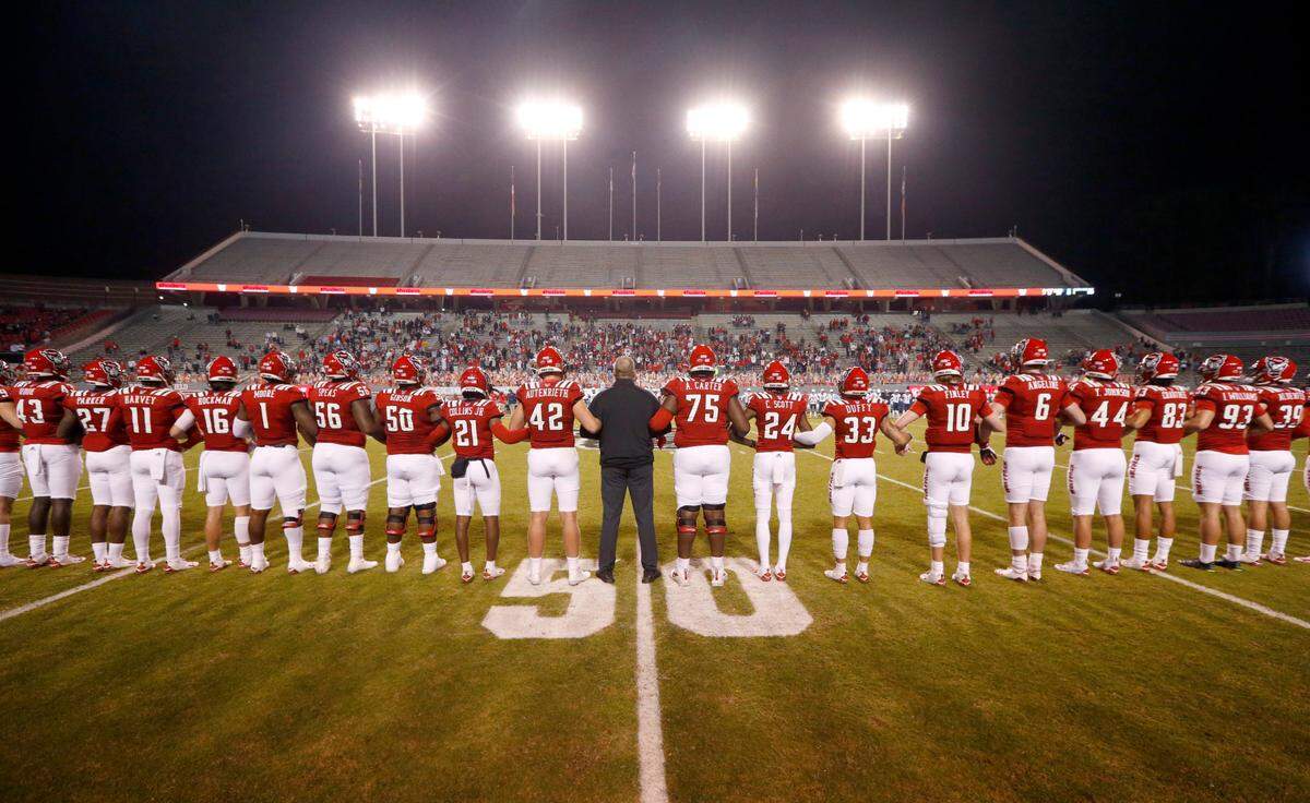 The Wolfpack players and coaches lock arms before N.C. State’s game against Liberty at Carter-Finley Stadium in Raleigh, N.C., Saturday, Nov. 21, 2020.