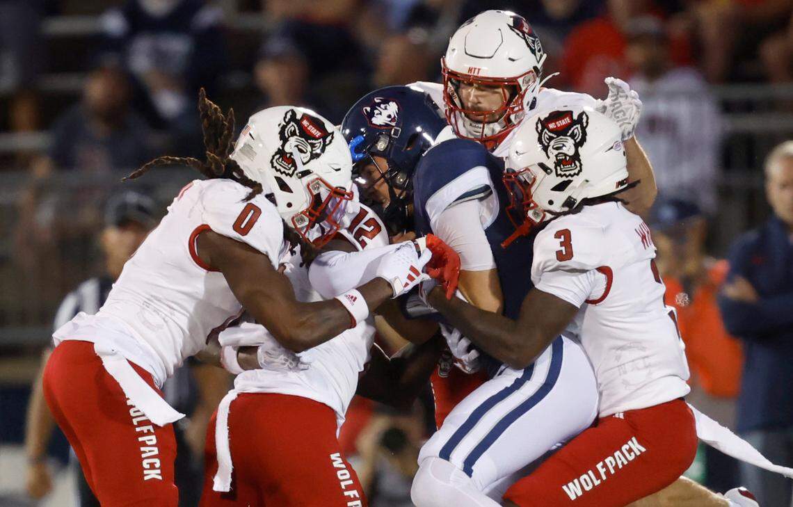 N.C. State’s Sean Brown (0), Devan Boykin (12), Payton Wilson (11) and Aydan White (3) wrap up Connecticut quarterback Joseph Fagnano (2) during the first half of N.C. State’s game against UConn at Rentschler Field in East Hartford, Conn. Thursday, August 31, 2023.