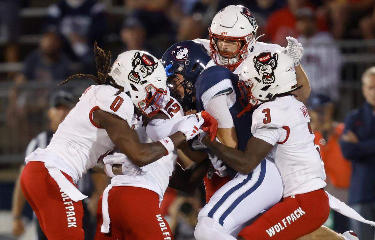 N.C. State’s Sean Brown (0), Devan Boykin (12), Payton Wilson (11) and Aydan White (3) wrap up Connecticut quarterback Joseph Fagnano (2) during the first half of N.C. State’s game against UConn at Rentschler Field in East Hartford, Conn. Thursday, August 31, 2023.