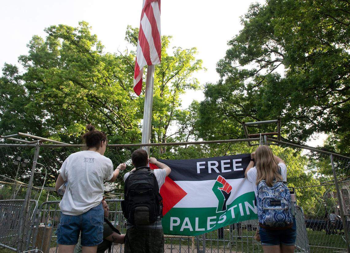People attach a “Free Palestine” flag to a fence barrier surrounding the flagpole on the campus of UNC-Chapel Hill on Tuesday, April 30, 2024. UNC-Chapel Hill police charged 36 members of a pro-Palestinian “Gaza solidarity encampment” Tuesday morning after warning the group to remove its tents from campus or face possible arrest, suspension or expulsion from the university.