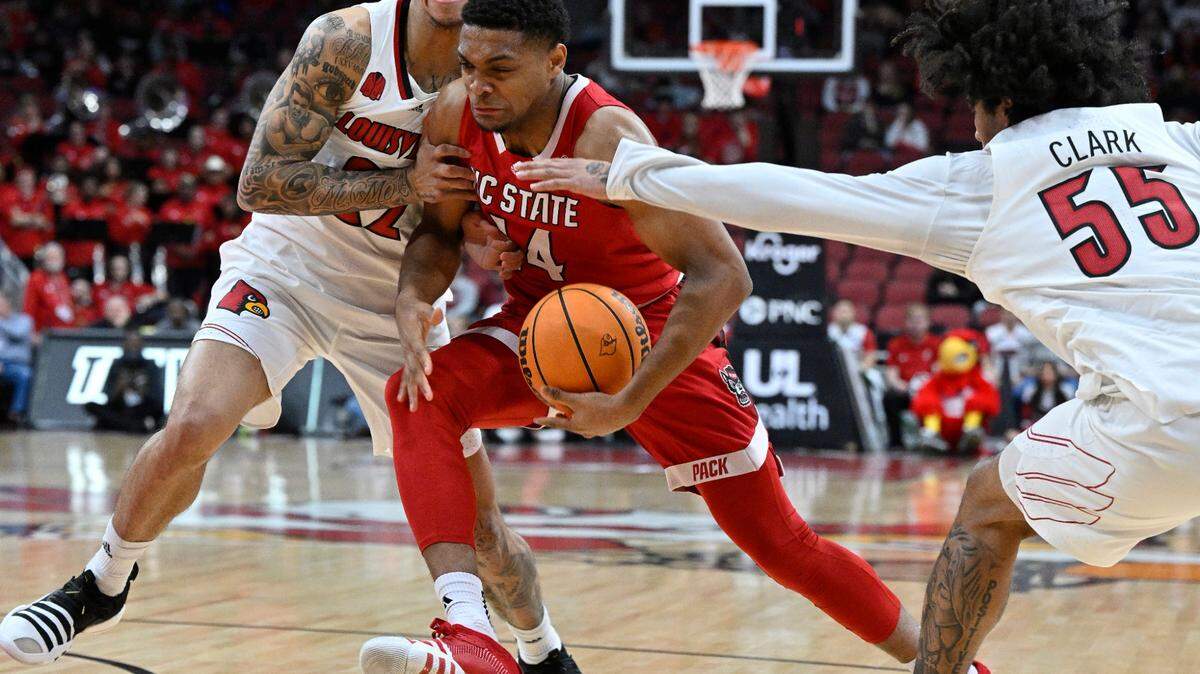 Jan 13, 2024; Louisville, Kentucky, USA; North Carolina State Wolfpack guard Casey Morsell (14) drives to the basket against Louisville Cardinals guard Tre White (22) and guard Skyy Clark (55) during the first half at KFC Yum! Center. Mandatory Credit: Jamie Rhodes-USA TODAY Sports