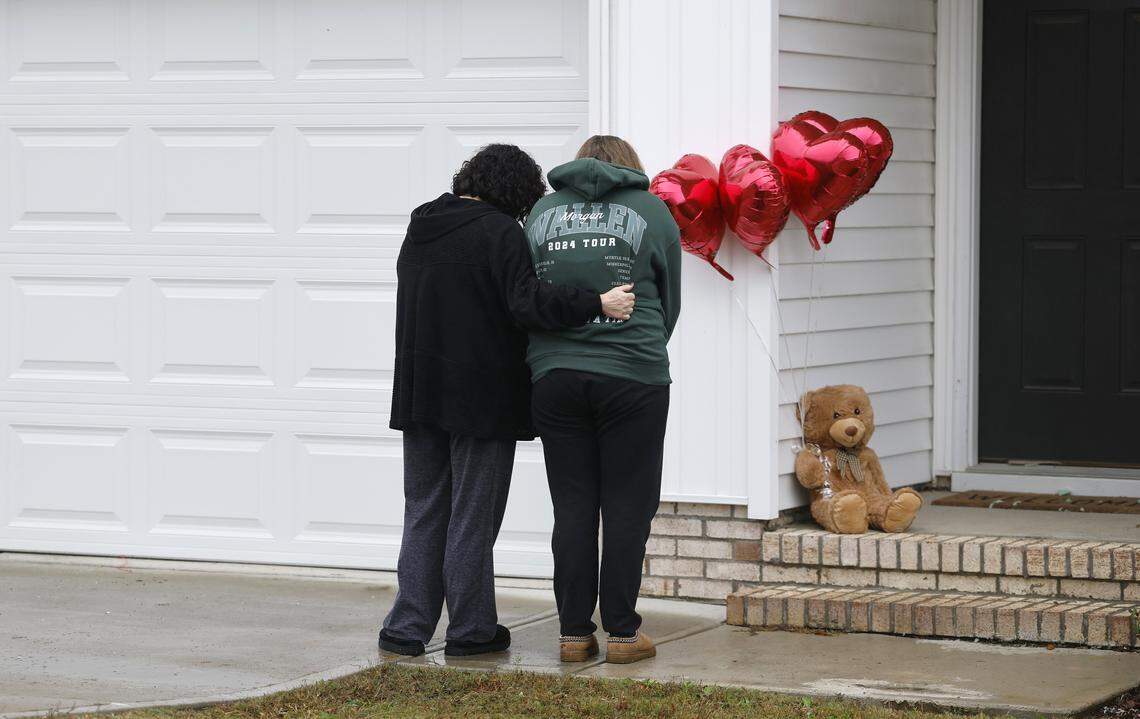 Rachel Ross and her mother Debra Riley bow their heads after placing a teddy bear and four balloons on the porch of the home of Wellington Dickens III in Zebulon, N.C., Wednesday, Oct. 29, 2025. Dickens faces four charges of murder in the deaths of his children 6-year-old Leah Dickens, 9-year-old Zoe Dickens, 10-year-old Wellington Dickens IV and 18-year-old Sean Brasfield, his stepson.