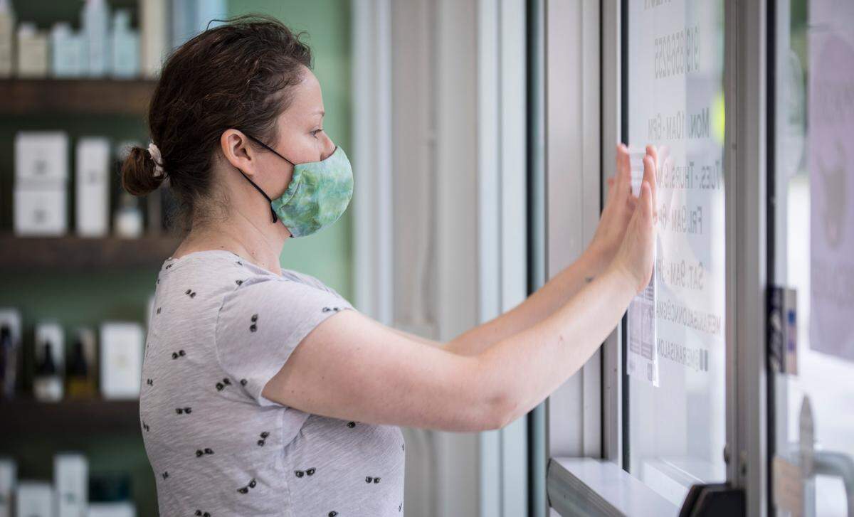 Michelle Ghassemi, owner of Meraki Salon in Raleigh, N.C., tapes a sign to the front doors of the salon about social distancing on Thursday, May 21, 2020. Ghassemi and her employees have been preparing to open at 50% capacity since Governor Roy Cooper announced on Wednesday that hair salons are included in Phase Two of re-opening North Carolina.