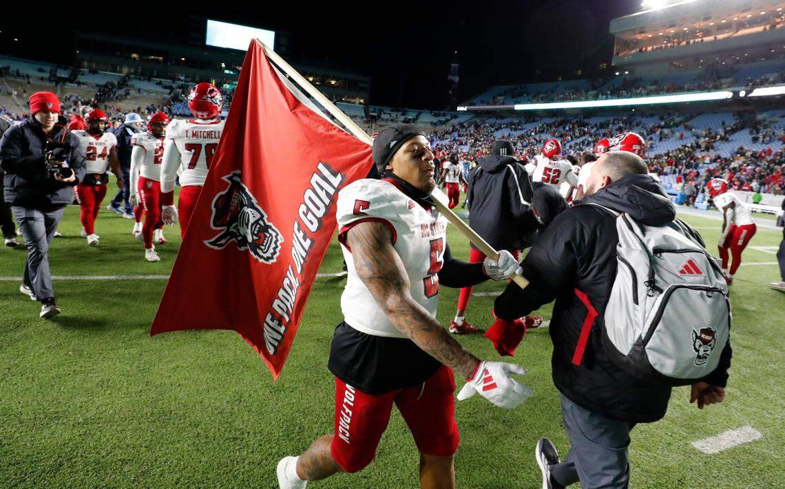 N.C. State’s DK Kaufman (5) walks the field with a Wolfpack flag after N.C. State’s 35-30 victory over UNC at Kenan Stadium in Chapel Hill, N.C., Saturday, Nov. 30, 2024.