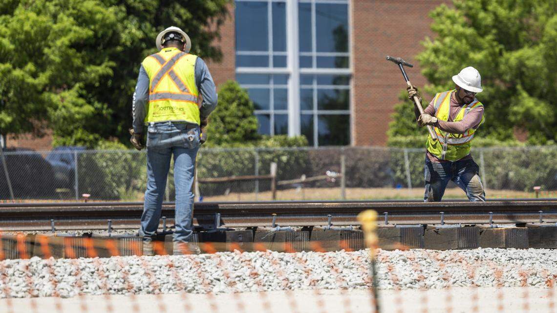 Workers install permanent railroad tracks where an underpass is under construction at the intersection of Blue Ridge Road, Hillsborough Street and Beryl Road near the N.C. State Fairgrounds in Raleigh on Wednesday, April 15, 2026.