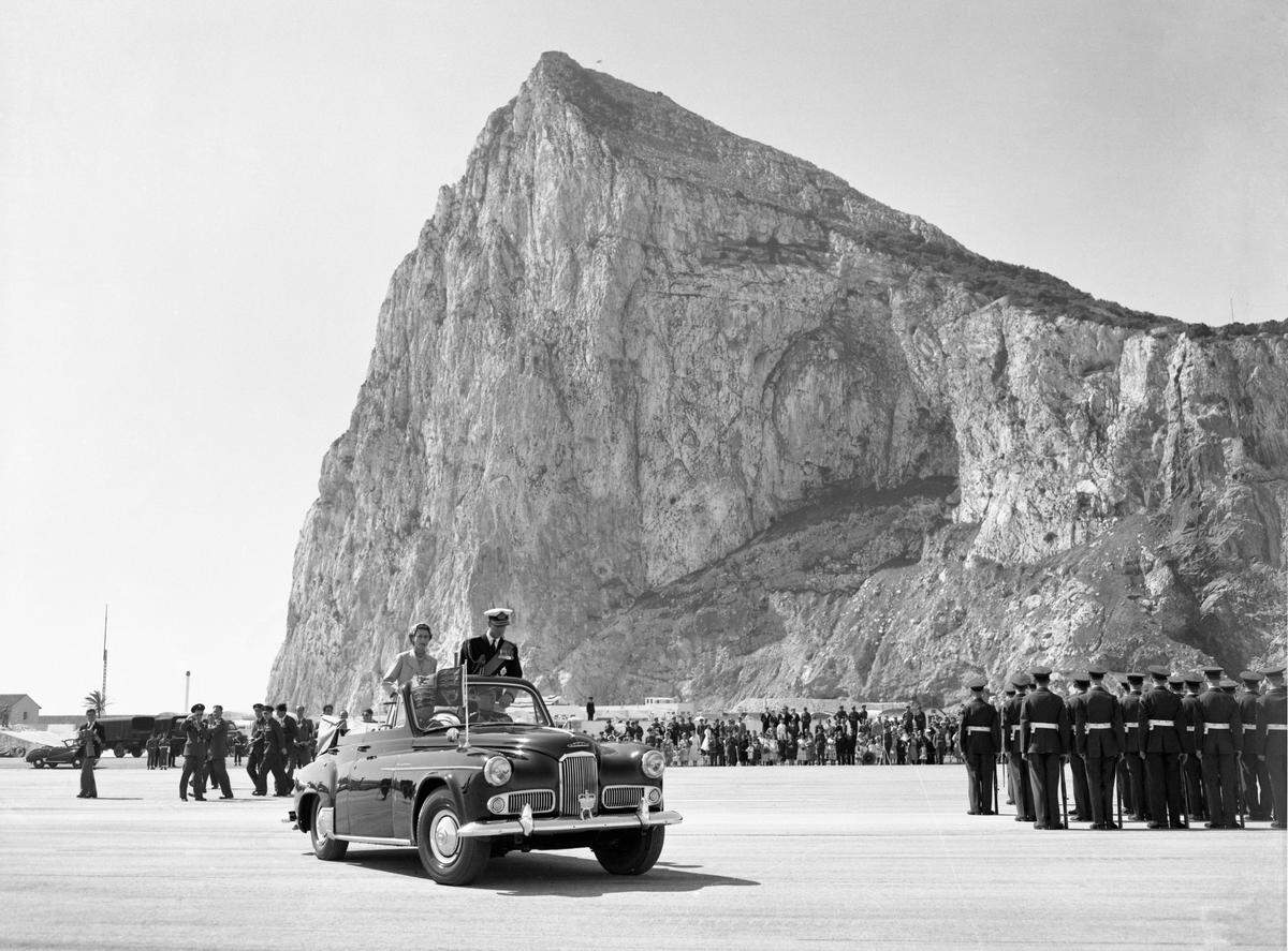 The Rock towers over Britain’s Queen Elizabeth II, and the Duke of Edinburgh drive past the assembled ranks of troops and lines of bombers, during a review of the services at North Front Airfield after they had arrived in Gibraltar, on May 10, 1954.