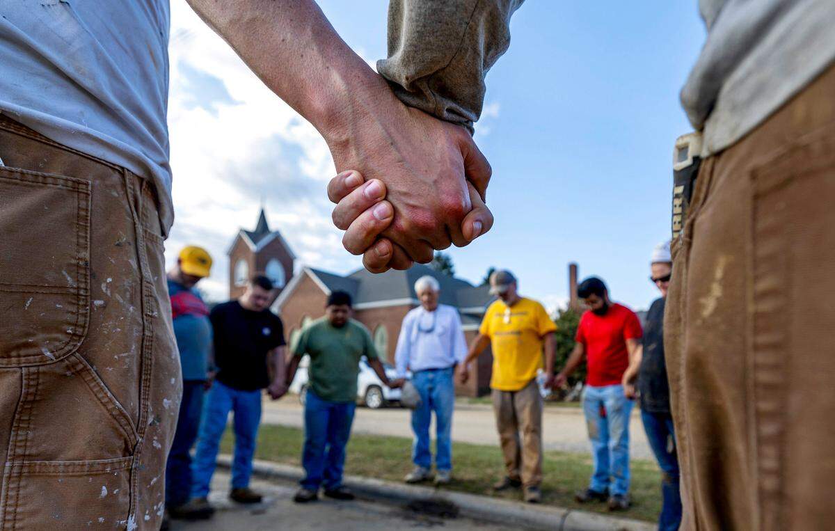 Members of IChurch from Hickory, N.C. pray with Bob Smith, center, a Trustee of the Old Fort United Methodist Church on Saturday, October 5, 2024 in Old Fort, N.C. More than four feet of water from Mill Creek flooded the building during Hurricane Helene. IChurch members volunteered their time on Saturday to shovel mud, and salvage items from the building.