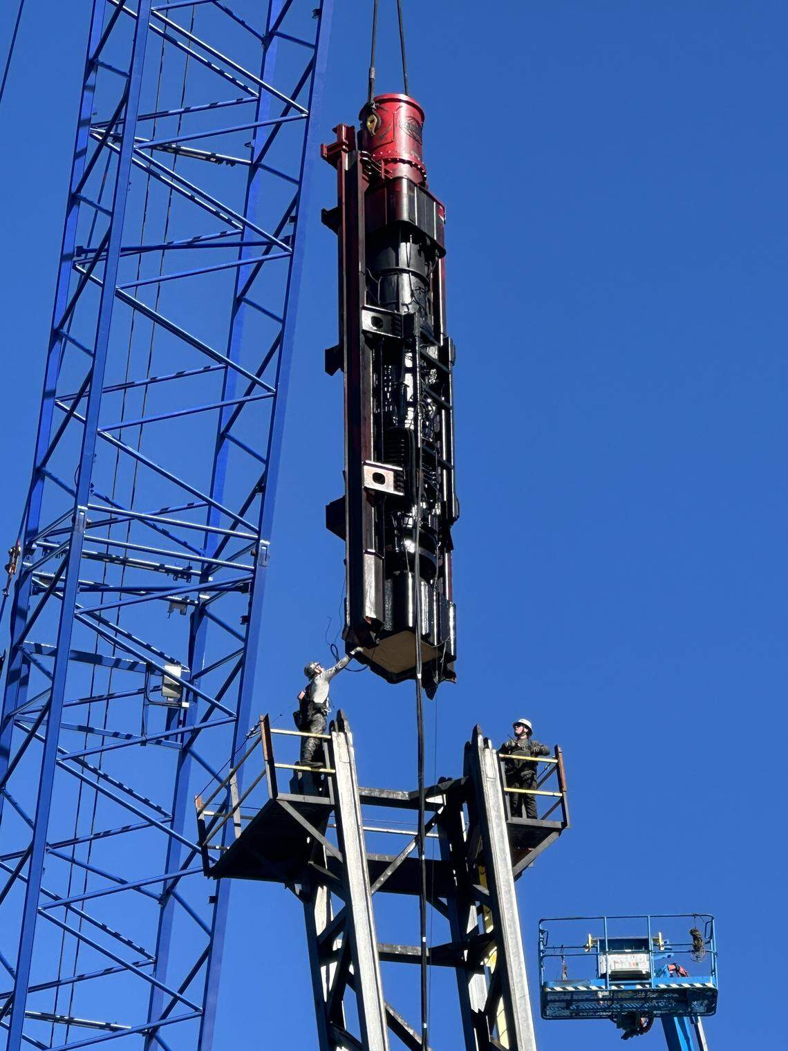 Workers help guide a 40,000-pound power hammer that will be used to drive a concrete pile into the Alligator River.